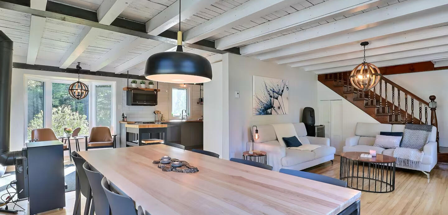 Aire ouverte du chalet Le Monarque près de Magog avec salon, salle à manger et cuisine moderne Salon et salle à manger lumineux du chalet Le Monarque près de Magog avec cuisine ouverte et grande table en bois pour 8 personnes